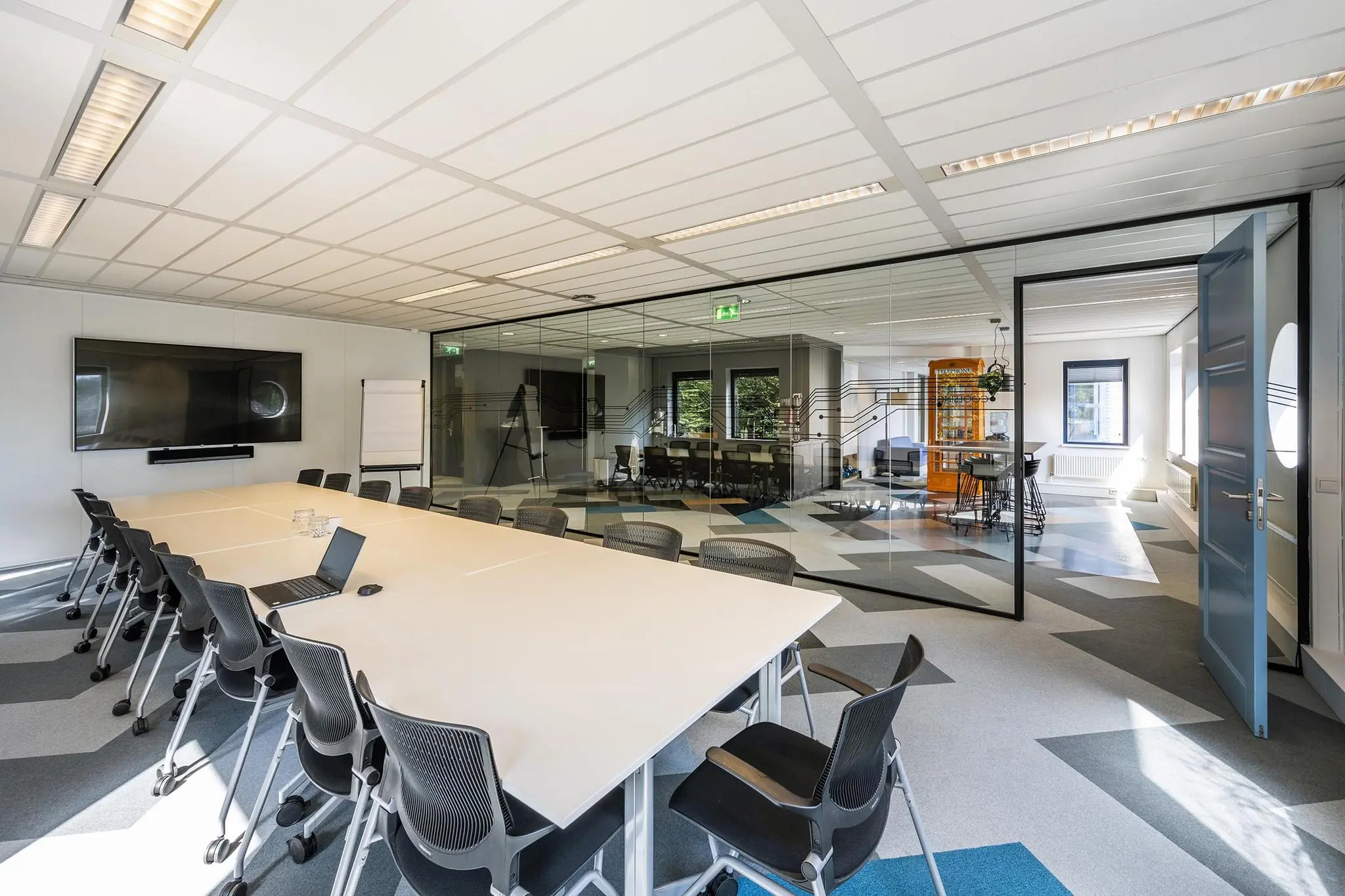 Moderne vergaderruimte aan de Amersfoortseweg met een lange tafel, glazen wand en doorkijk naar een loungegedeelte.