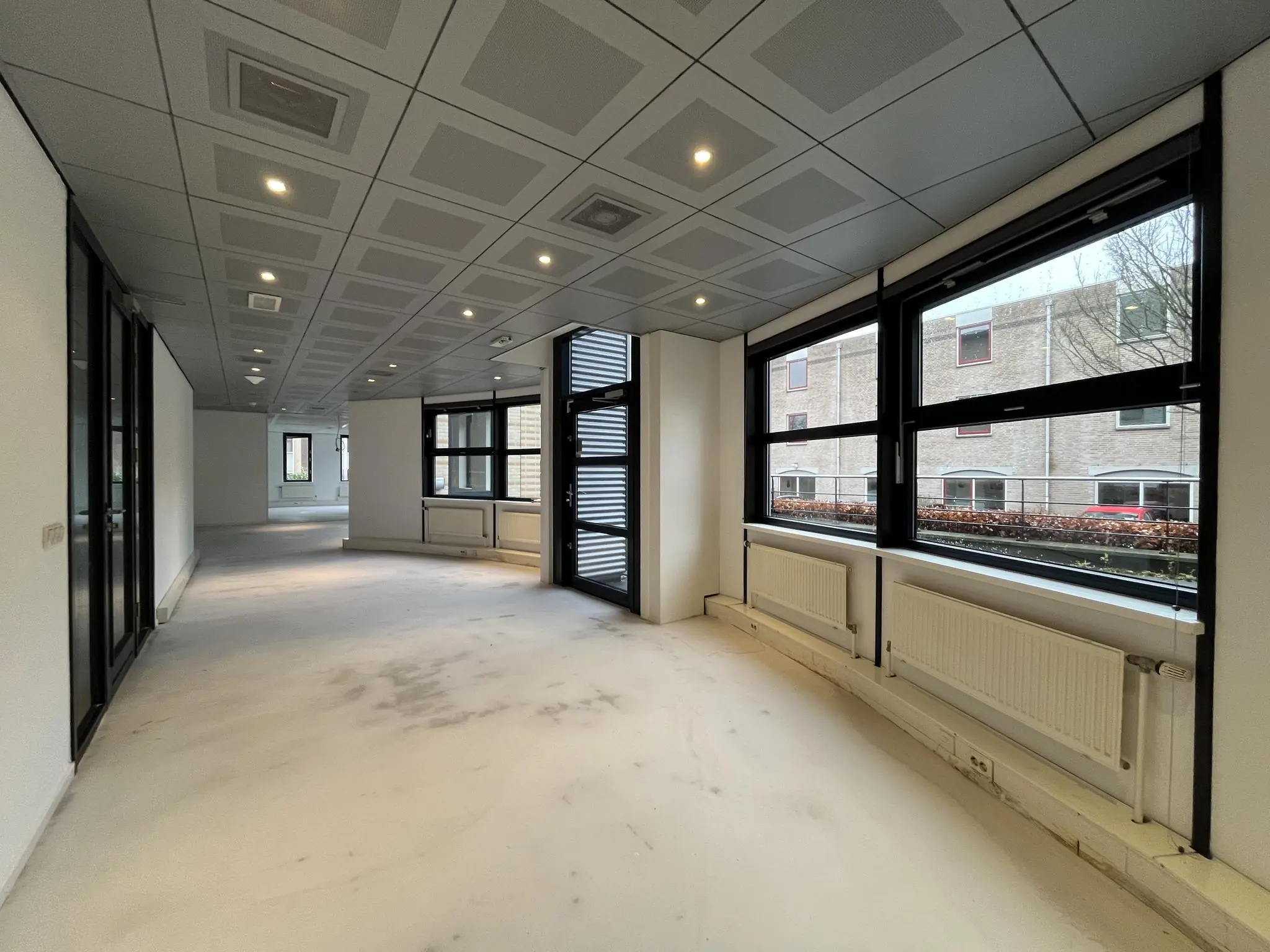 Leeg kantoorpand aan de Amersfoortseweg met grote ramen, systeemplafond en witte muren.