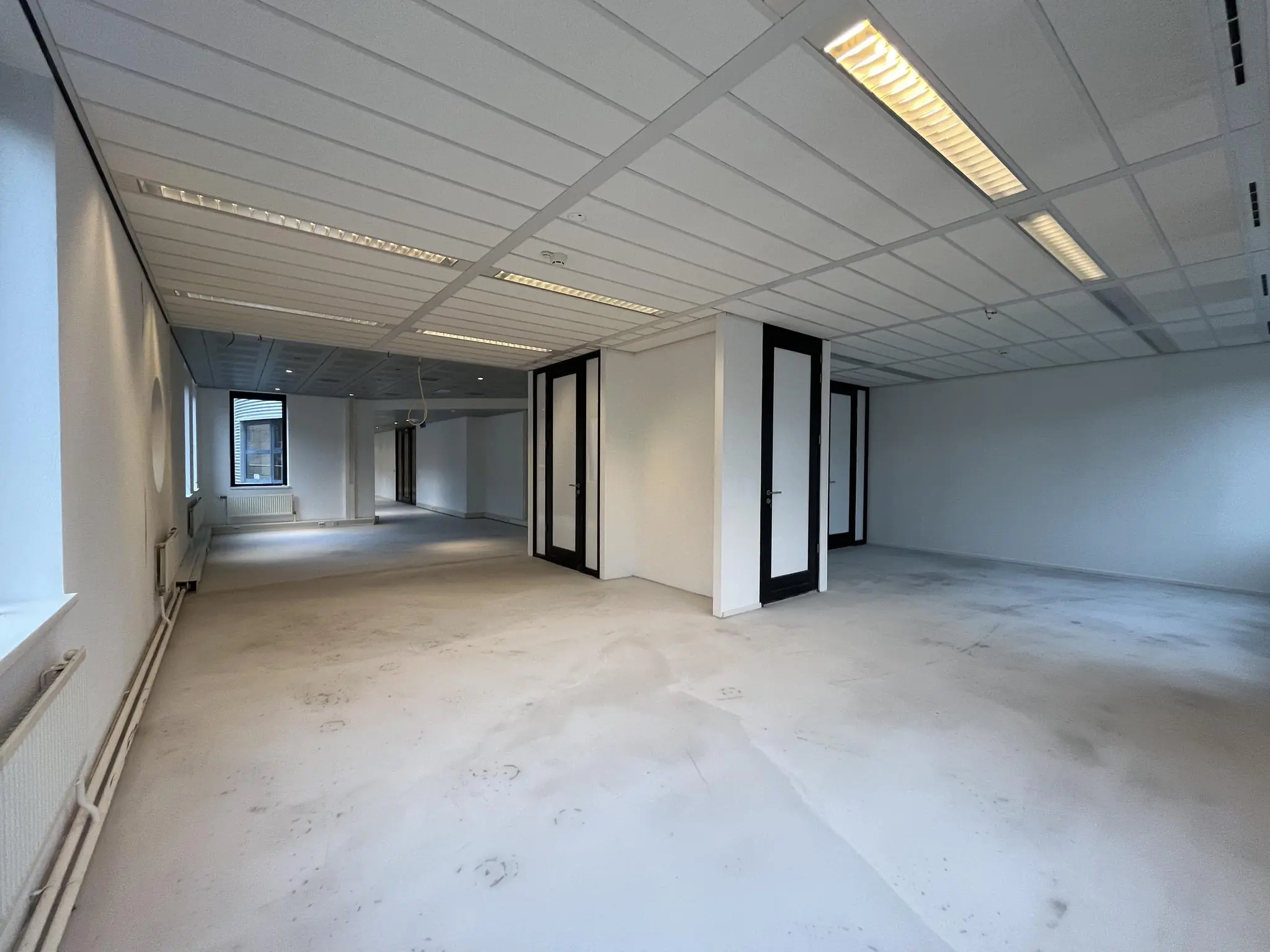Leegstaand kantoorpand aan de Amersfoortseweg met witte muren, systeemplafond en meerdere glazen deuren.