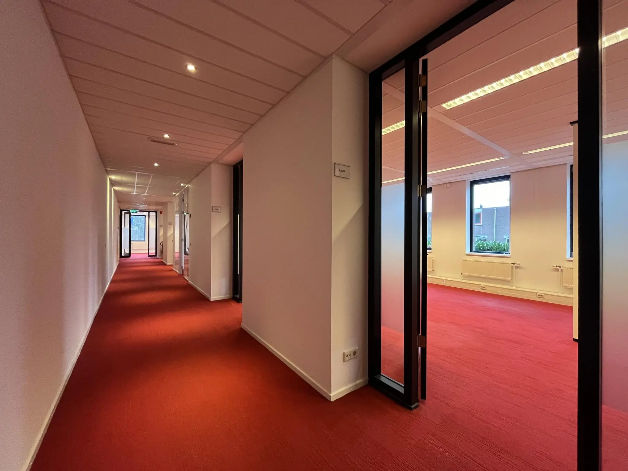 Gang met rood tapijt en openstaande kantoordeuren in een kantoorpand aan de Amersfoortseweg.