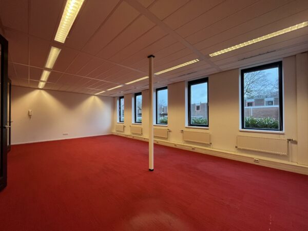 Leeg kantoorruimte aan de Amersfoortseweg met rood tapijt, witte wanden en grote ramen met uitzicht op een woonwijk.