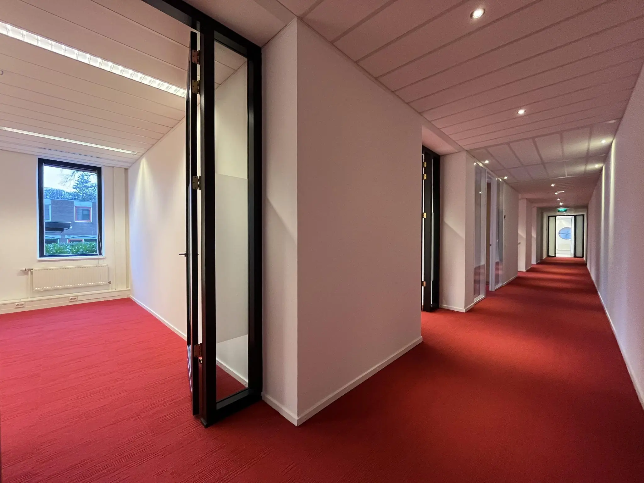 Gang met rode vloerbedekking en kantoorruimtes aan de Amersfoortseweg.