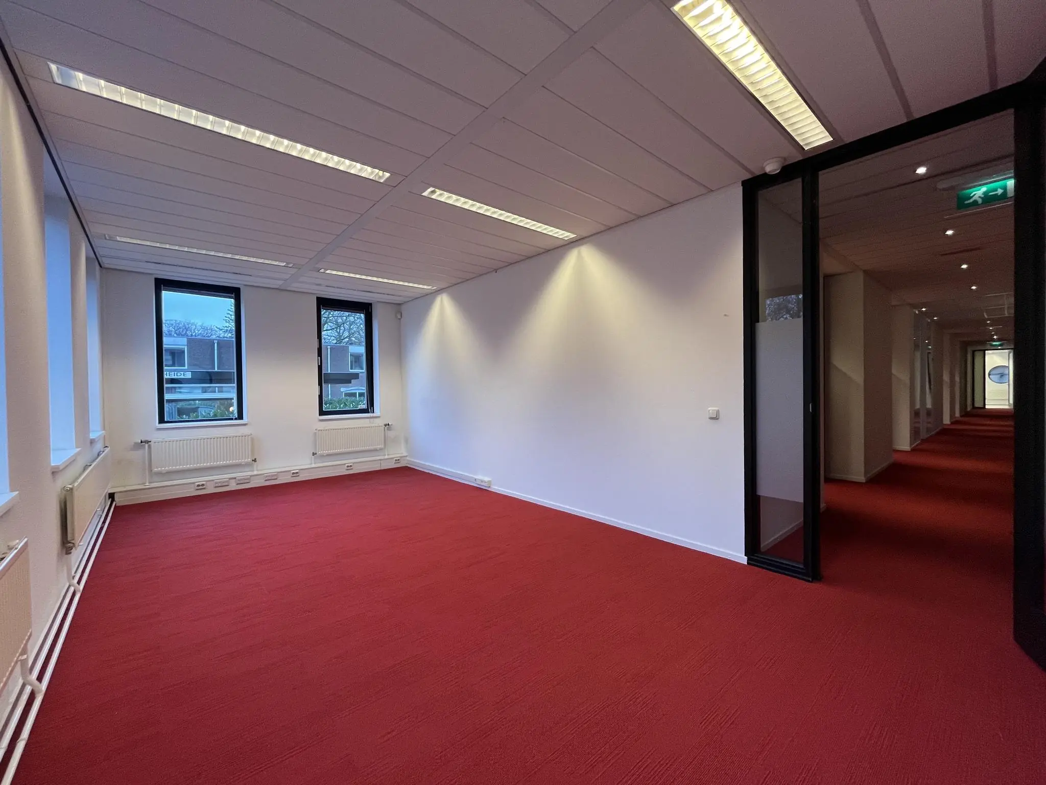 Leeg kantoorpand aan de Amersfoortseweg met rode vloerbedekking, witte muren en twee ramen die uitkijken op een woonwijk.