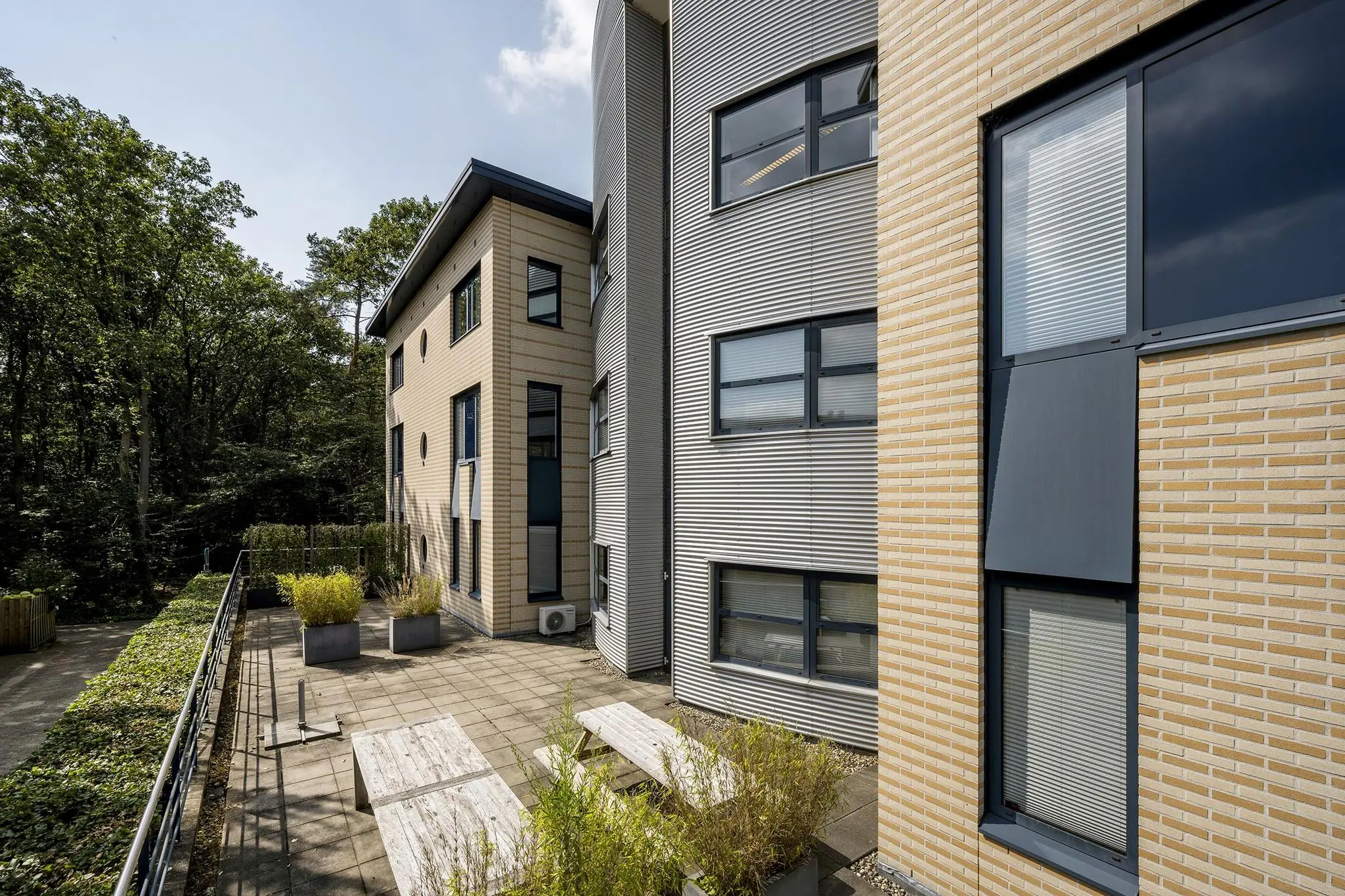 Modern kantoorpand aan de Amersfoortseweg met betegeld terras en omringende beplanting.