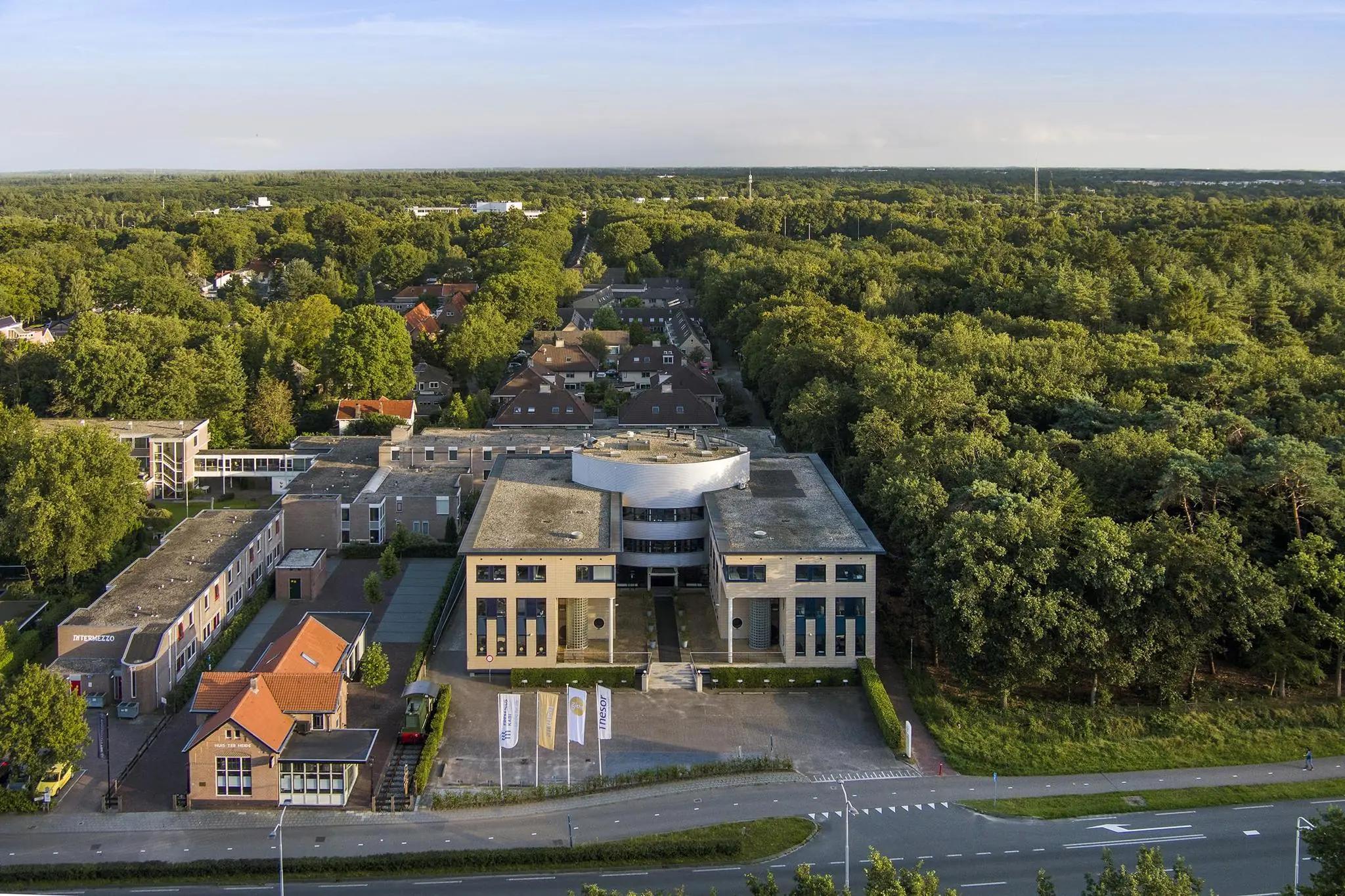 Luchtfoto van een modern kantoorgebouw aan de Amersfoortseweg, omringd door bos en woonhuizen.