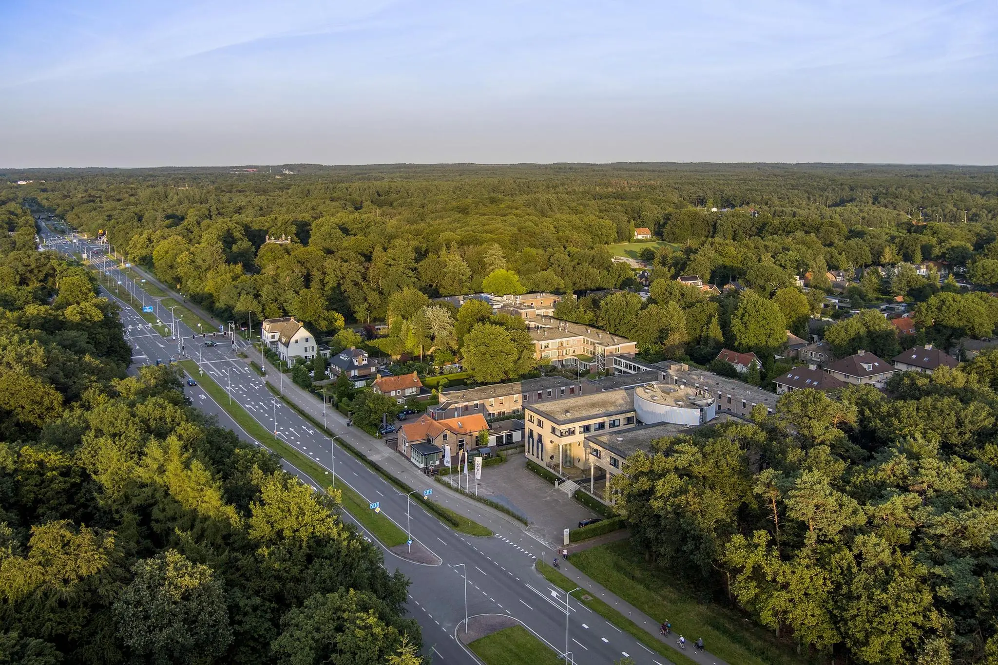 Luchtfoto van de Amersfoortseweg in een groene, bosrijke omgeving met woningen en gebouwen.