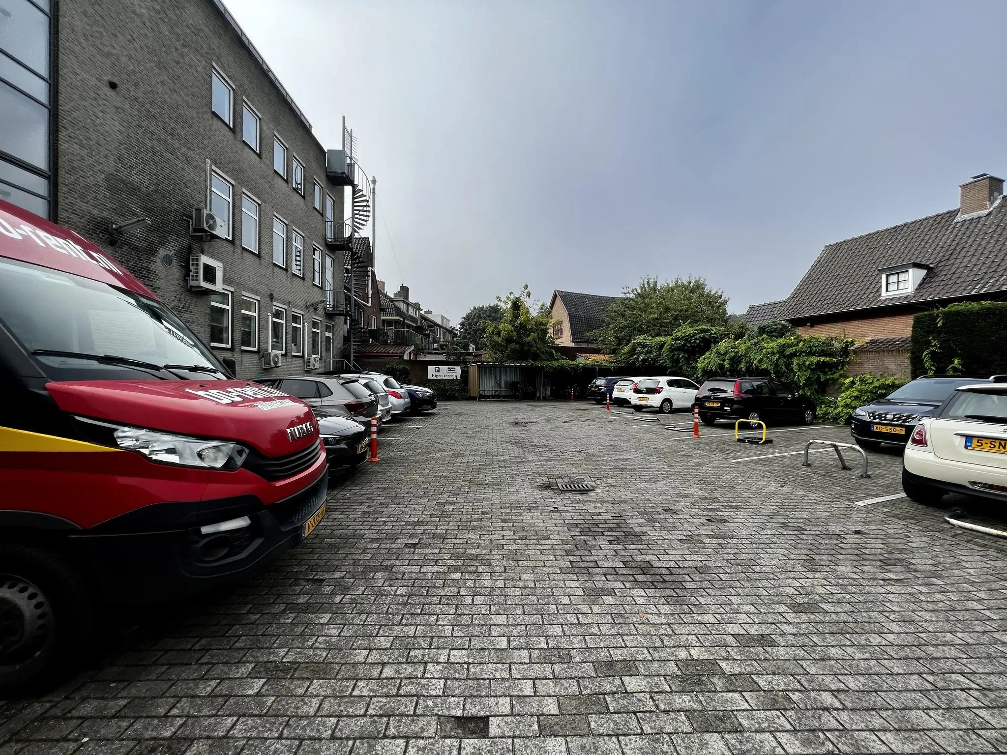 Parkeerterrein aan de Utrechtseweg met geparkeerde auto's naast een bakstenen kantoorgebouw en woonhuizen.