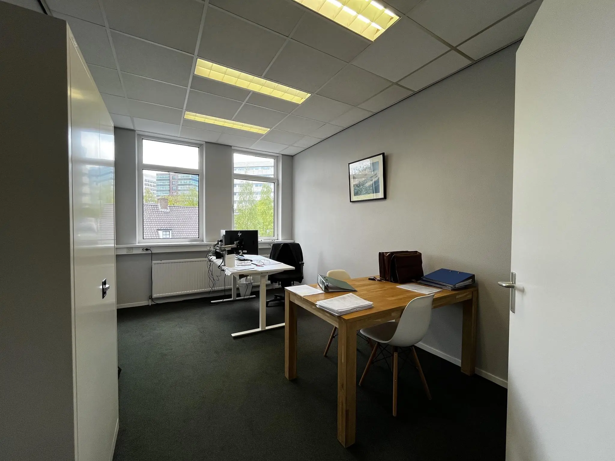Kleine, moderne kantoorruimte aan de Utrechtseweg met twee bureaus, computers en uitzicht op kantoorgebouwen buiten.