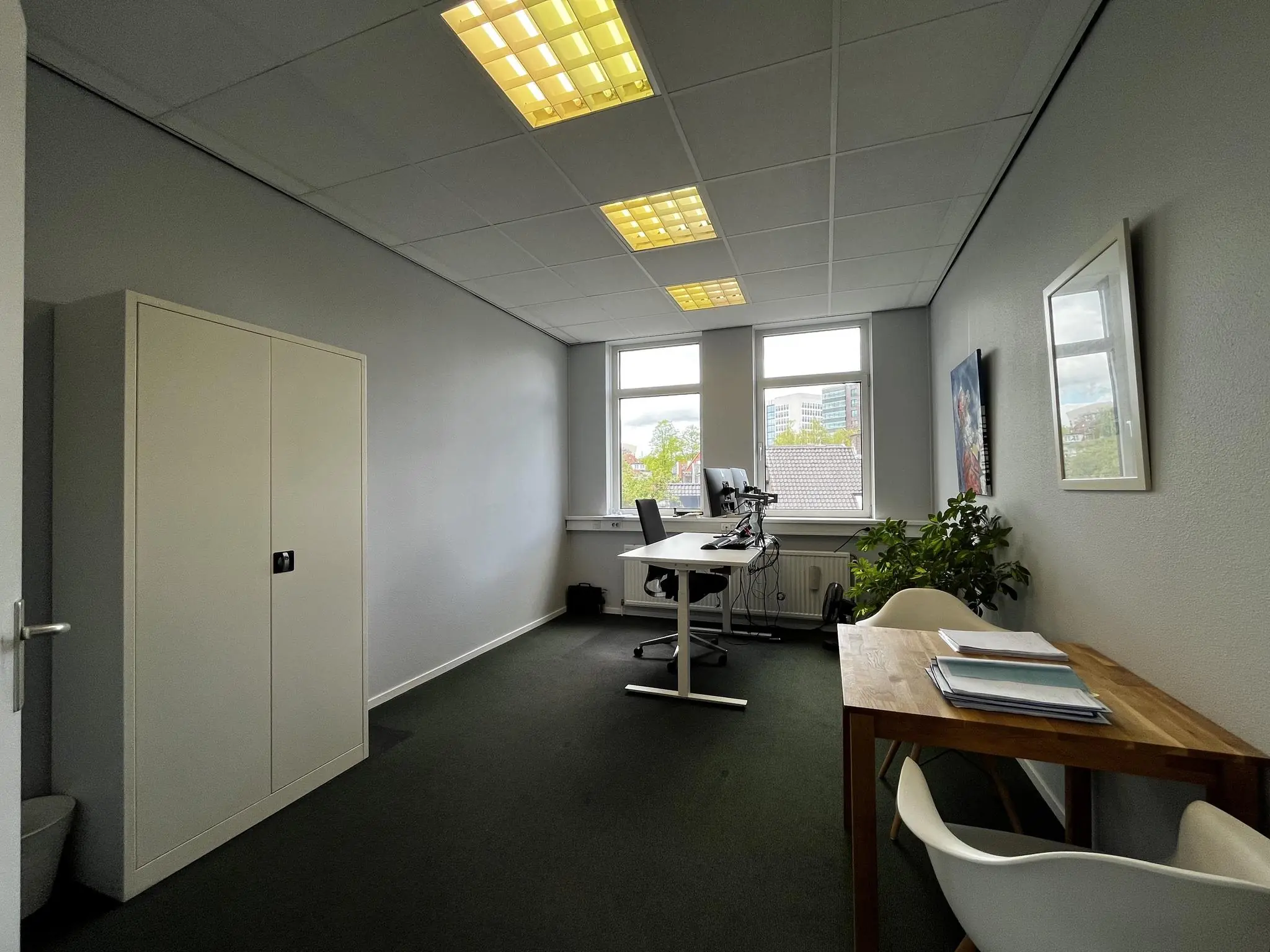 Modern kantoor aan de Utrechtseweg met een zit-sta bureau, opbergkast, vergadertafeltje en uitzicht op kantoorpanden.
