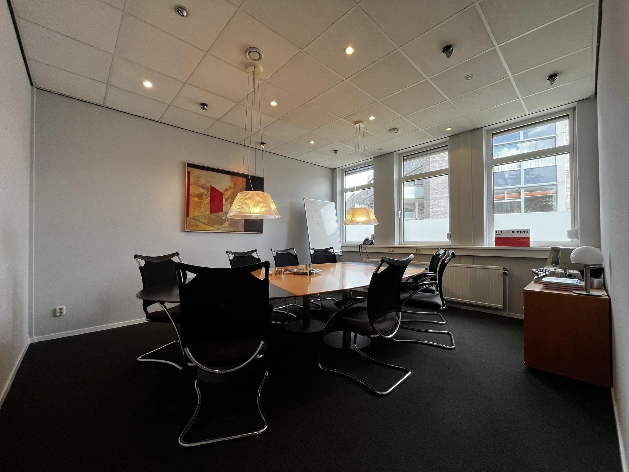 Vergaderruimte aan de Utrechtseweg met ovale tafel, acht stoelen, kunst aan de muur en grote ramen met daglicht.