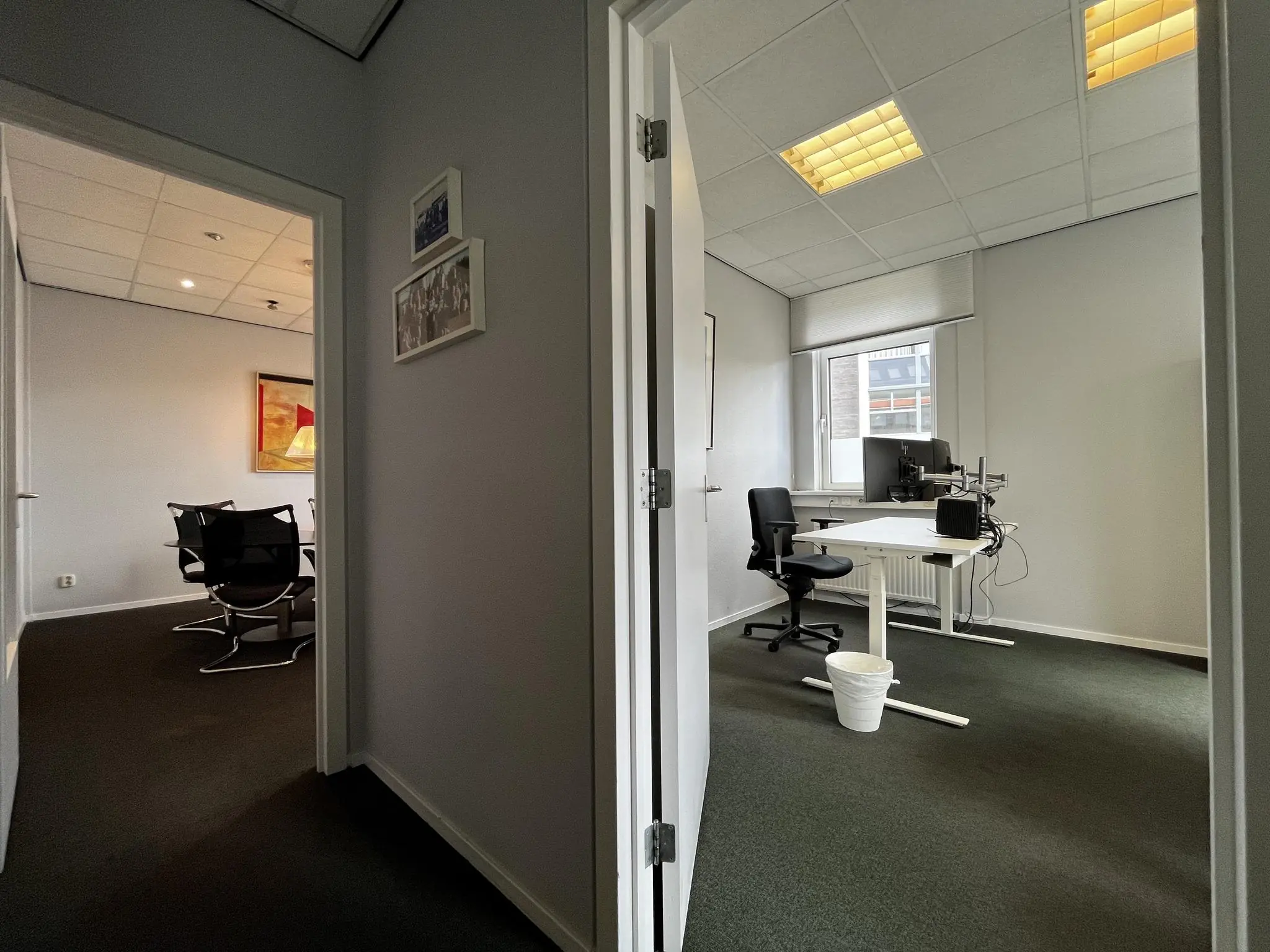 Kantoorruimte aan de Utrechtseweg met een vergaderruimte links en een werkplek met bureau en bureaustoel rechts.