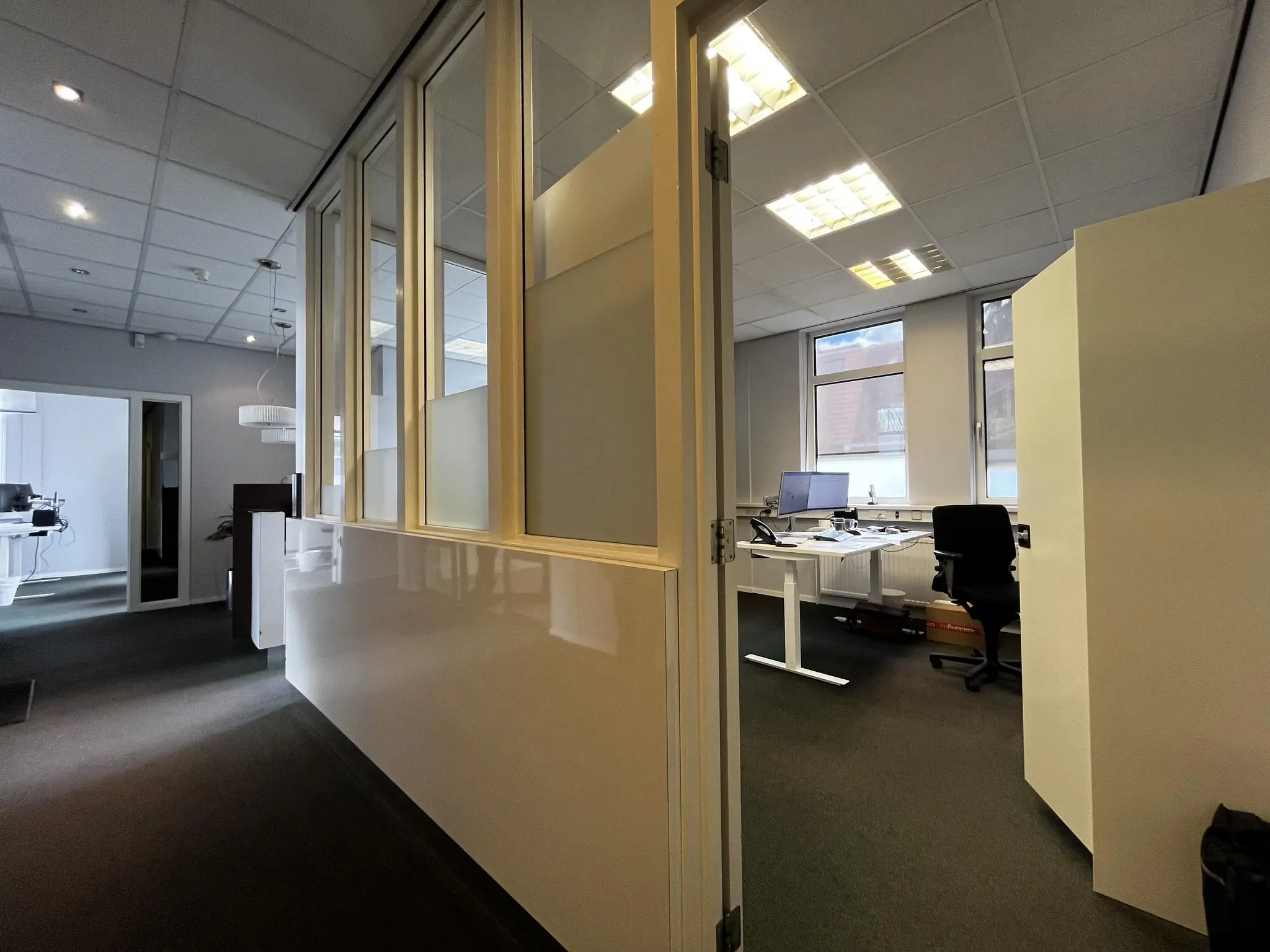 Modern kantoorinterieur aan de Utrechtseweg met openstaande deur naar een werkruimte met bureaus en computers.
