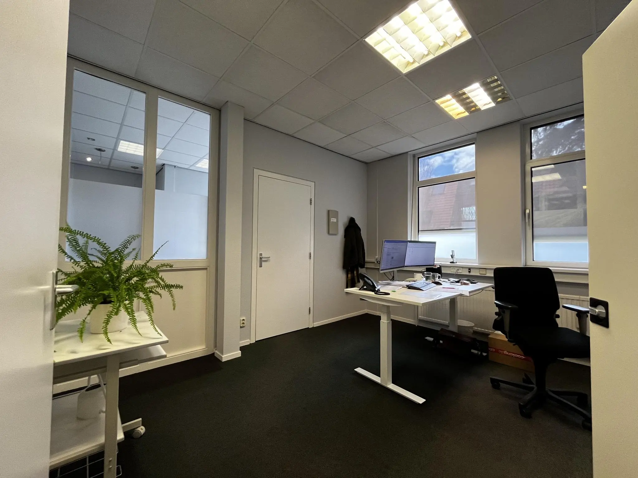 Modern kantoor aan de Utrechtseweg met bureau, bureaustoel, beeldscherm en grote ramen.