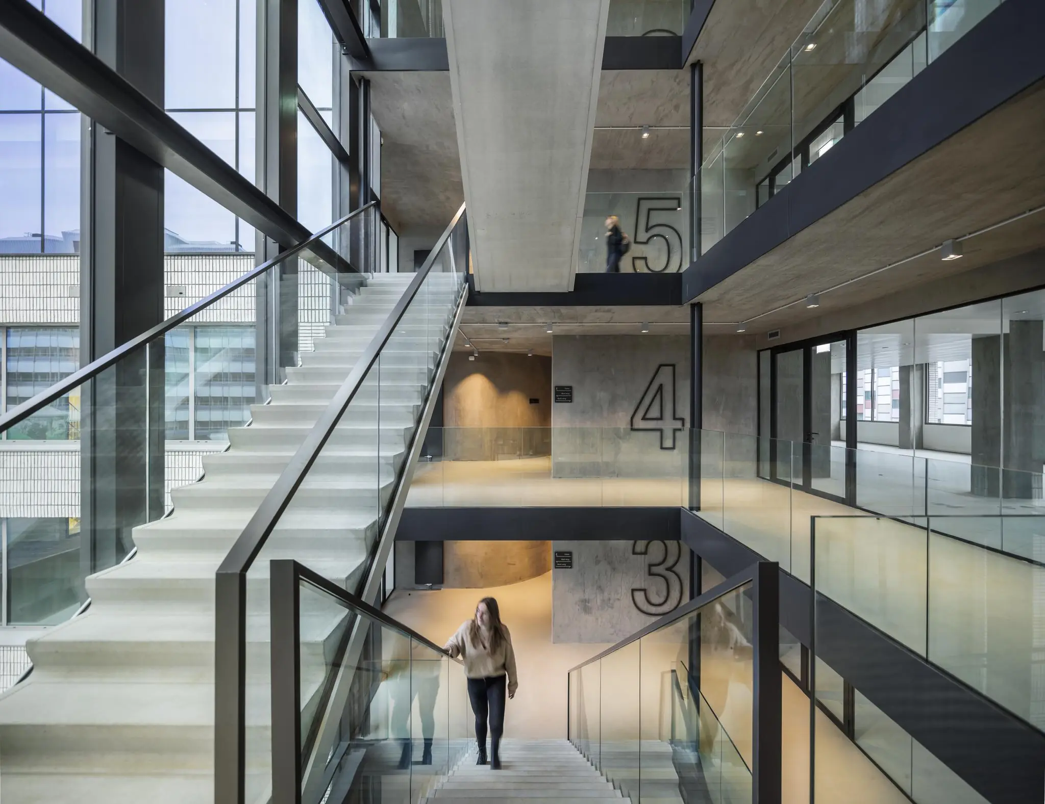 Modern interieur van het Catharijnesingel-gebouw met betonnen trappenhuis, glazen balustrades en zicht op meerdere verdiepingen.