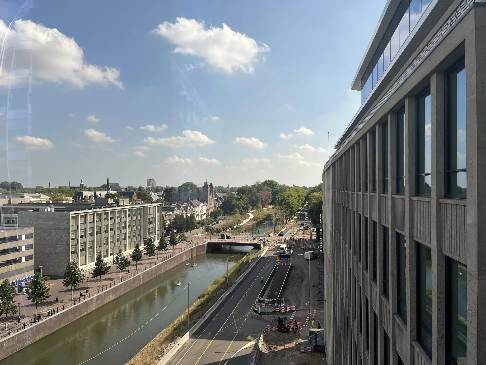 Uitzicht op de Catharijnesingel in Utrecht met het kanaal, een weg, en omliggende gebouwen op een zonnige dag.