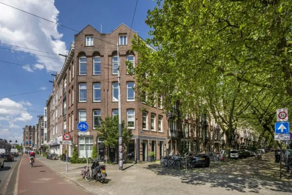 Straatbeeld van de Lomanstraat in Amsterdam met rode bakstenen panden, geparkeerde fietsen en een groene boomrijke laan.