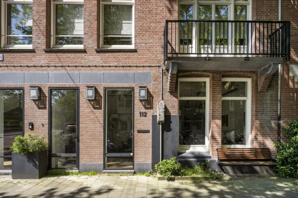 Vooraanzicht van een modern gerenoveerde bakstenen gevel aan de Lomanstraat, met huisnummer 112, een balkon en een houten bankje.