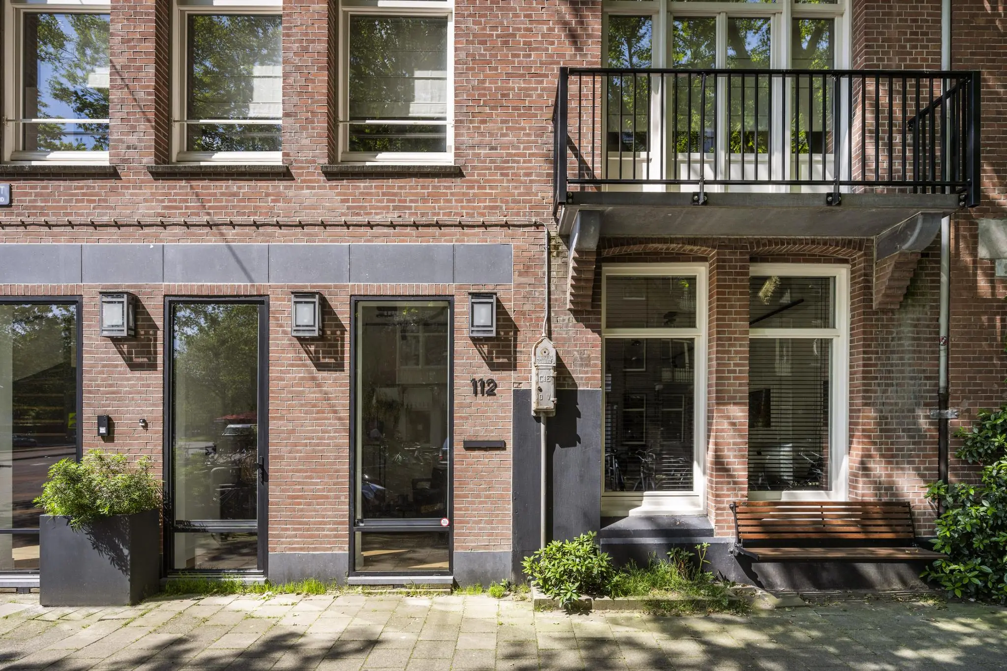 Vooraanzicht van een modern gerenoveerde bakstenen gevel aan de Lomanstraat, met huisnummer 112, een balkon en een houten bankje.