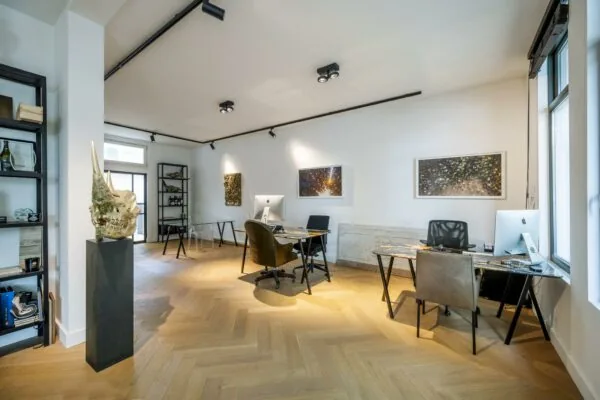 Modern ingericht kantoor aan de Lomanstraat met houten visgraatvloer, designmeubilair en kunst aan de muur.