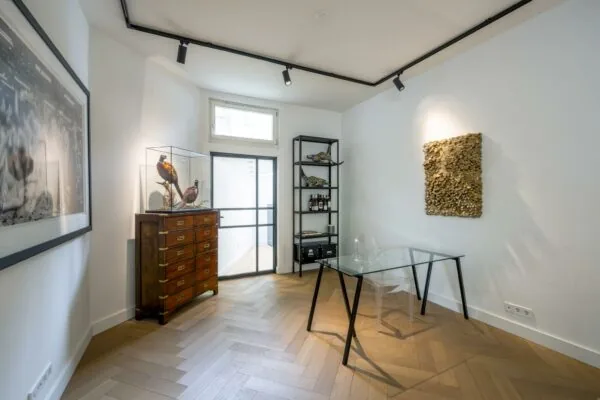 Modern ingerichte werkkamer aan de Lomanstraat met glazen bureau, kunstobjecten en houten visgraatvloer.