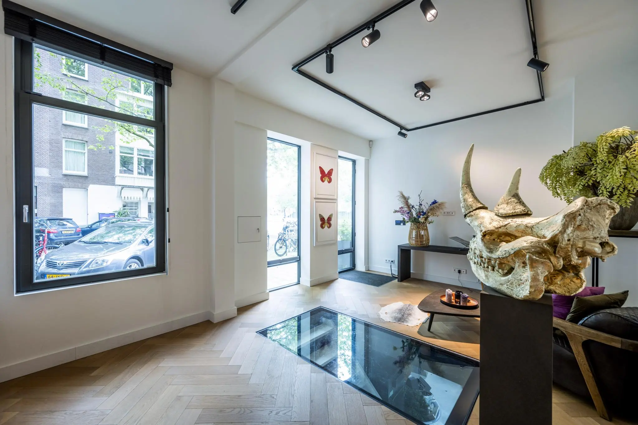 Moderne woonkamer aan de Lomanstraat met een glazen vloerpaneel, kunstobjecten en grote ramen met uitzicht op de straat.