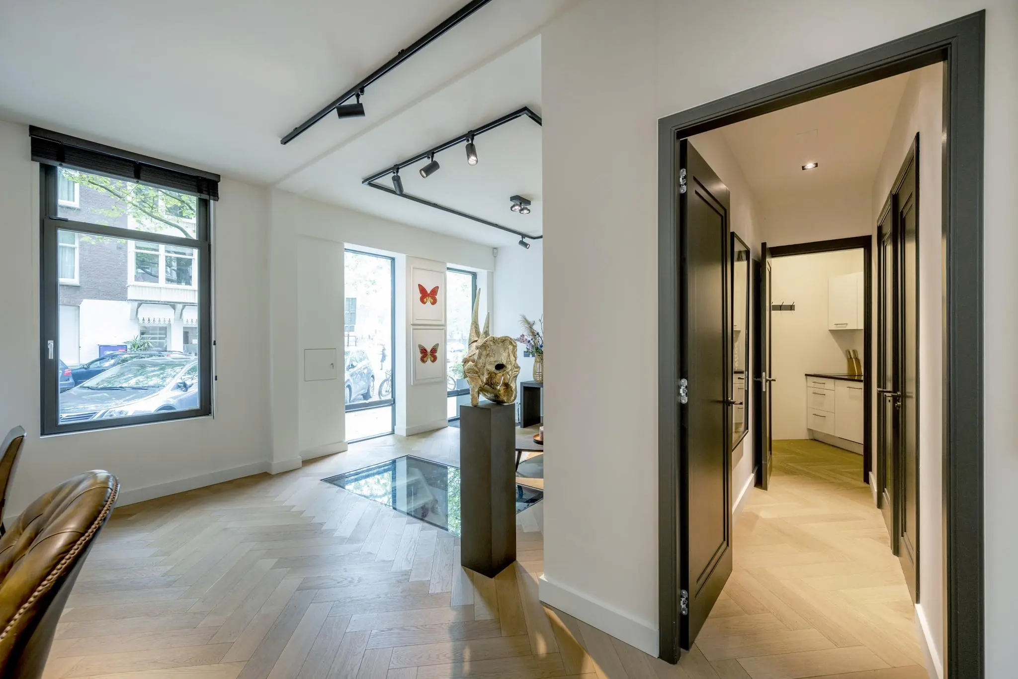 Moderne interieurruimte aan de Lomanstraat met houten visgraatvloer, kunst aan de muur en een doorkijk naar een keuken.