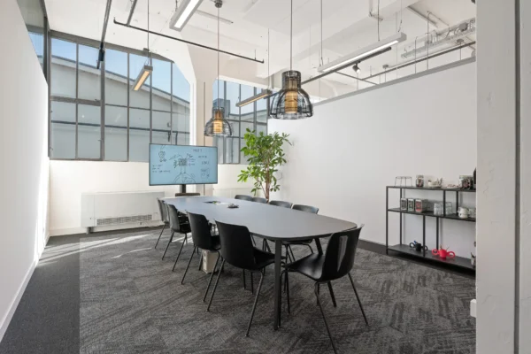 Een moderne vergaderruimte met een lange tafel, stoelen, een groot scherm en een plant bij het raam.