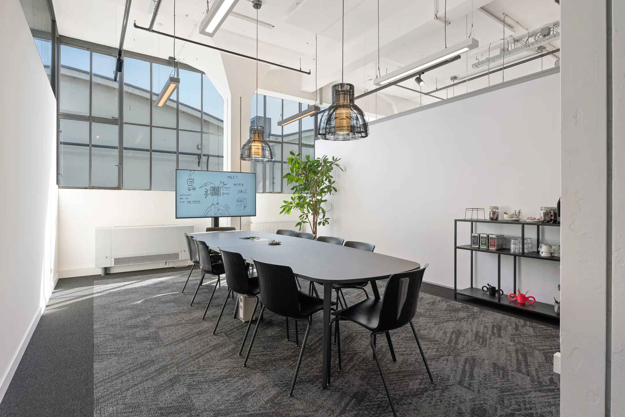 Een moderne vergaderruimte met een lange tafel, stoelen, een groot scherm en een plant bij het raam.