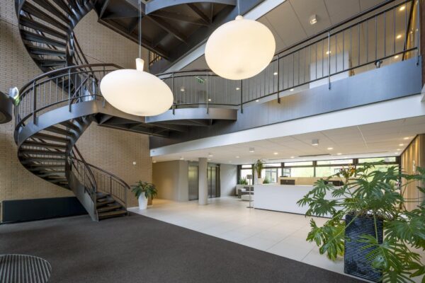 Moderne ontvangsthal aan de Amstelveenseweg met een zwarte wenteltrap, grote ronde hanglampen en een strakke witte receptiebalie.