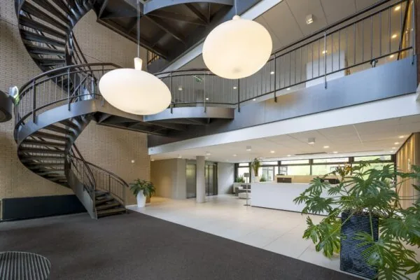Moderne ontvangsthal aan de Amstelveenseweg met een zwarte wenteltrap, grote ronde hanglampen en een strakke witte receptiebalie.