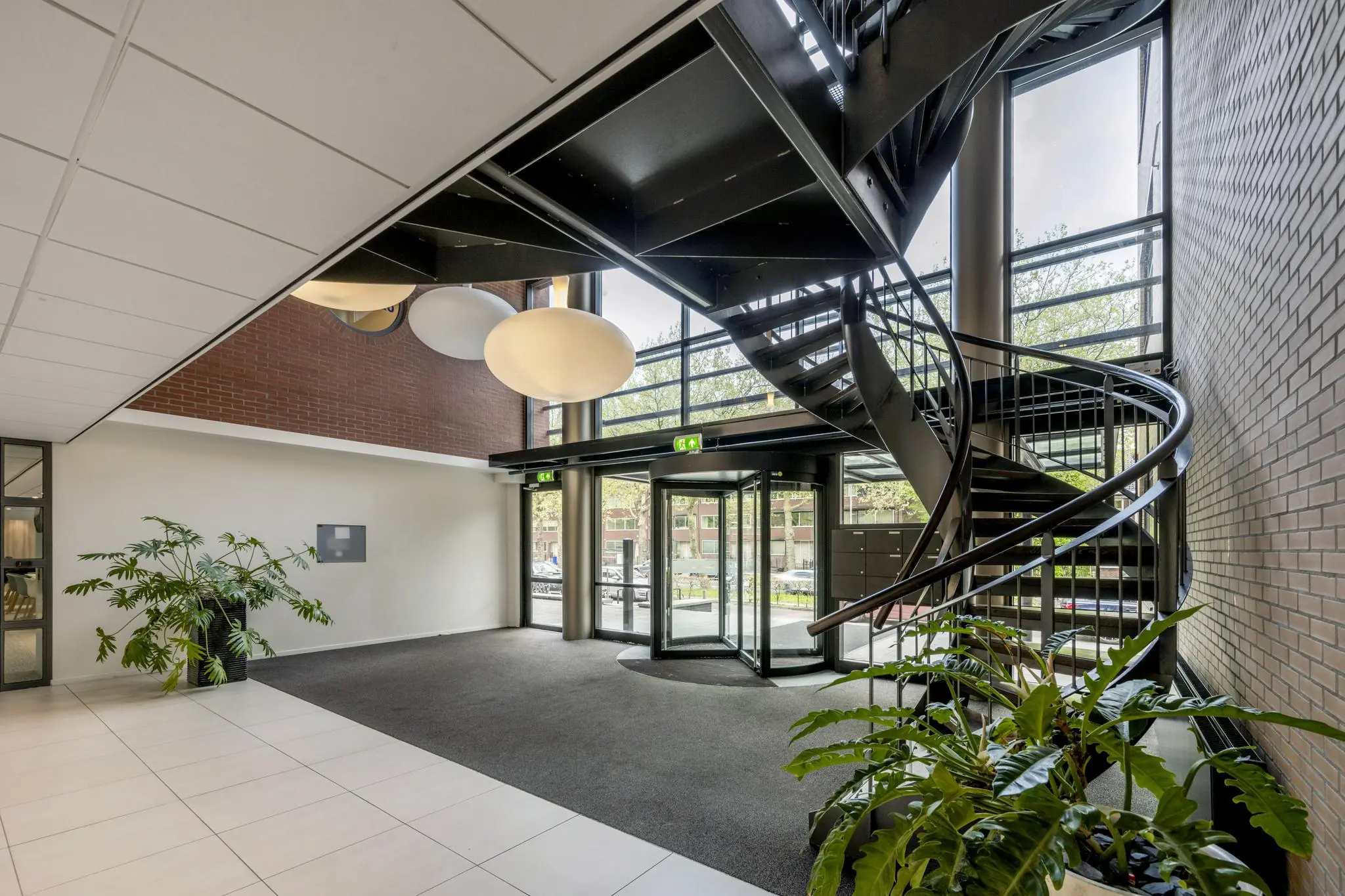 Moderne entreehal van een kantoorpand aan de Amstelveenseweg met een wenteltrap, grote ronde hanglampen en veel daglicht.
