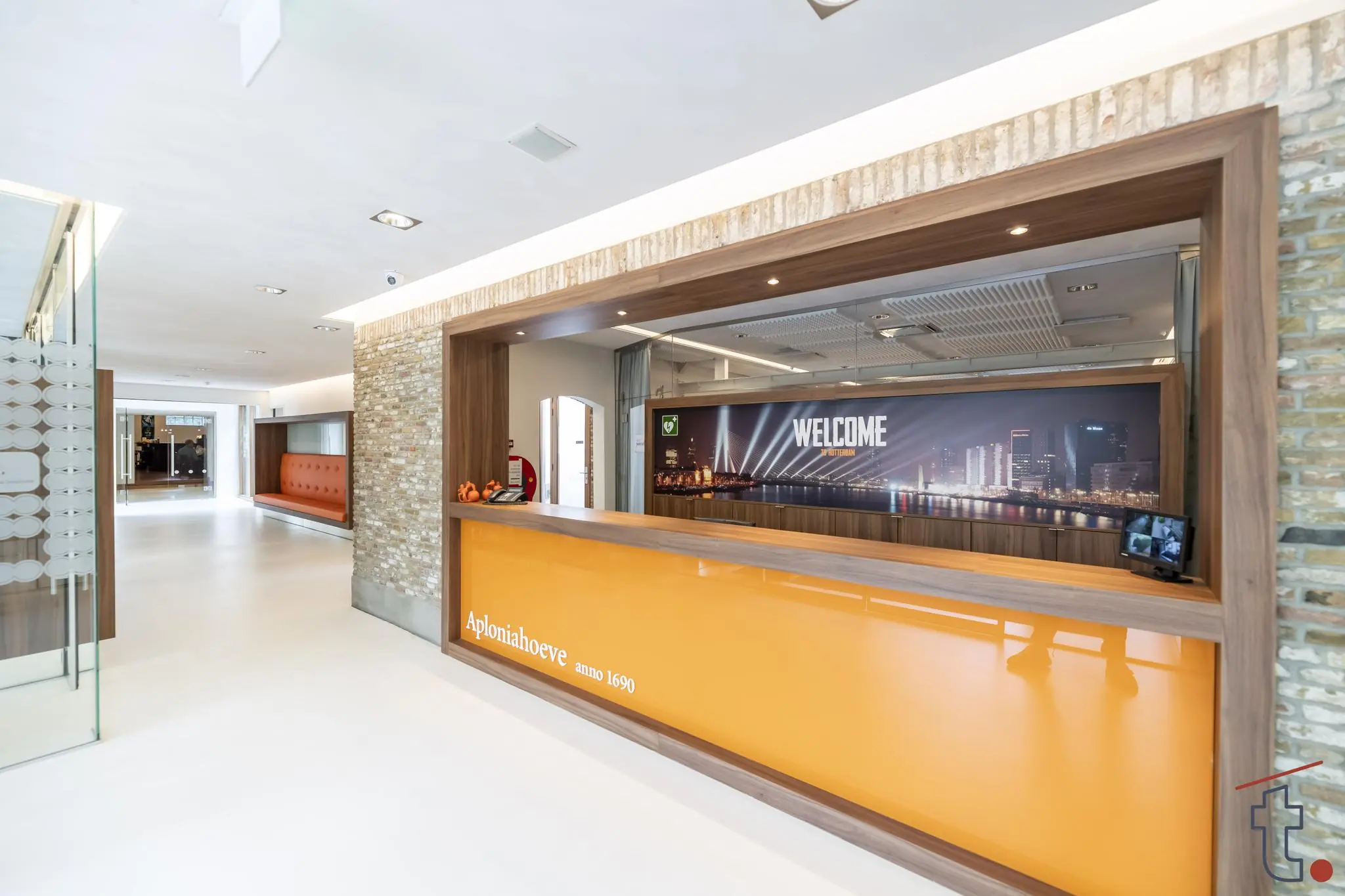 Moderne ontvangsthal van Aploniahoeve met oranje balie en foto van de Rotterdamse skyline.