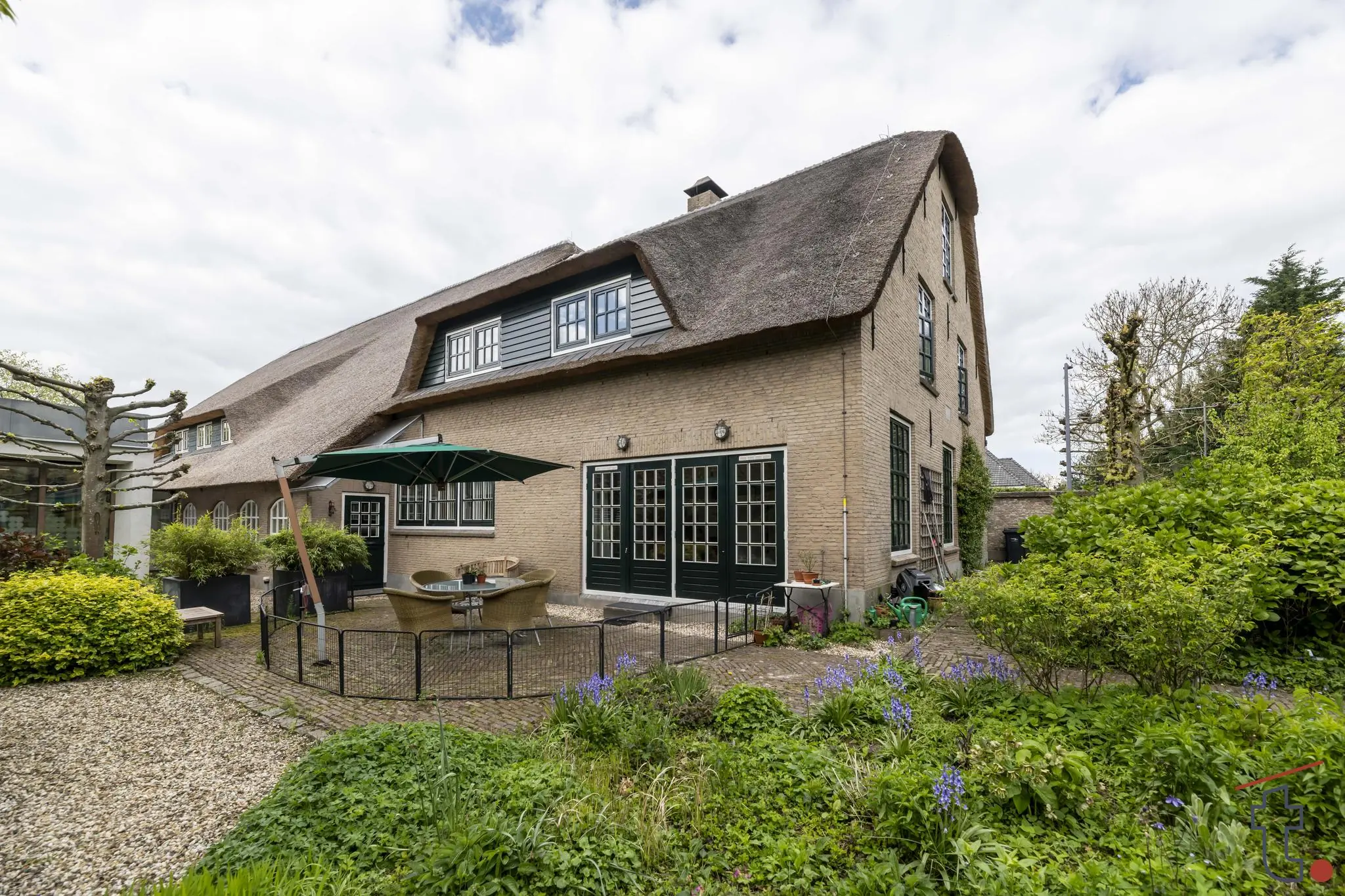 Rietgedekte woning aan de Charloisse Lagedijk met groene tuin en terras met parasol.