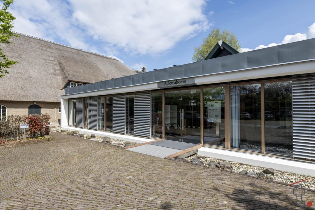 Moderne entree van woonzorgcentrum Aploniahoeve aan de Charloisse Lagedijk met deels rietgedekte boerderij op de achtergrond.