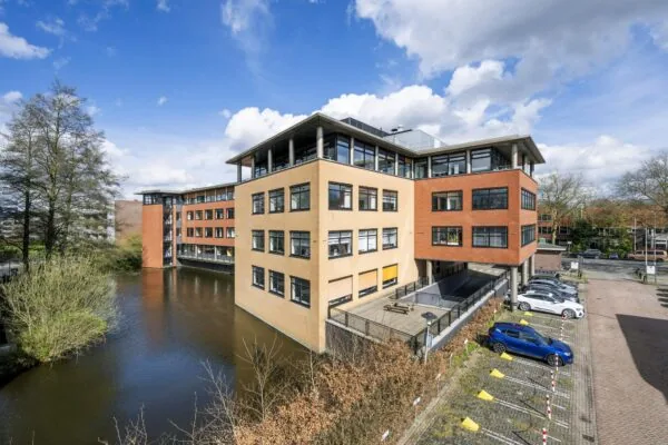Kantoorgebouw aan de Amstelveenseweg met parkeerplaatsen en een waterpartij, gezien op een zonnige dag.