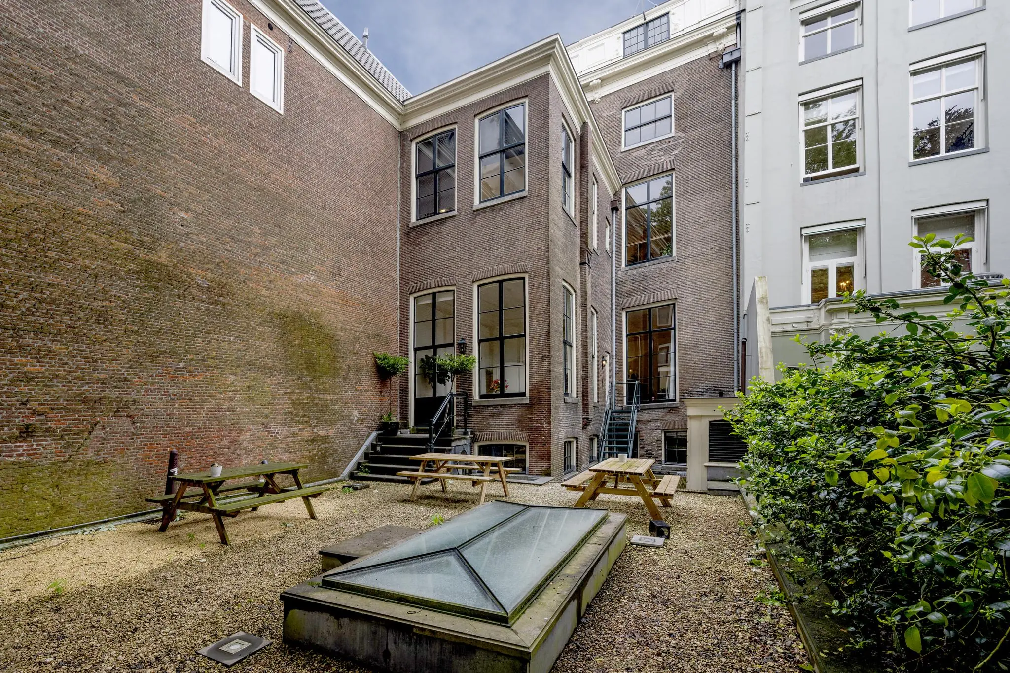 Binnenplaats van Herengracht 567 met picknicktafels, grindvloer en trappetjes naar de klassieke bakstenen gevels.