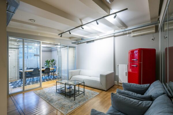 Moderne loungeruimte op Herengracht met grijze banken, een rode retro koelkast en glazen wand naar vergaderruimte.