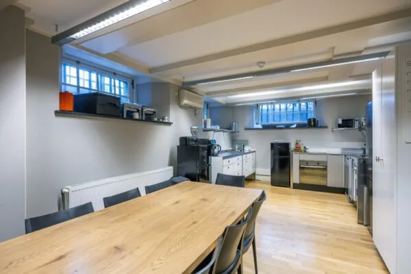 Moderne kantoorkeuken aan de Herengracht met houten eettafel, grijze stoelen en diverse keukenapparatuur.