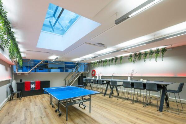 Moderne recreatieruimte aan de Herengracht met een tafeltennistafel, zithoek, bar, dartbord en plafondraam.