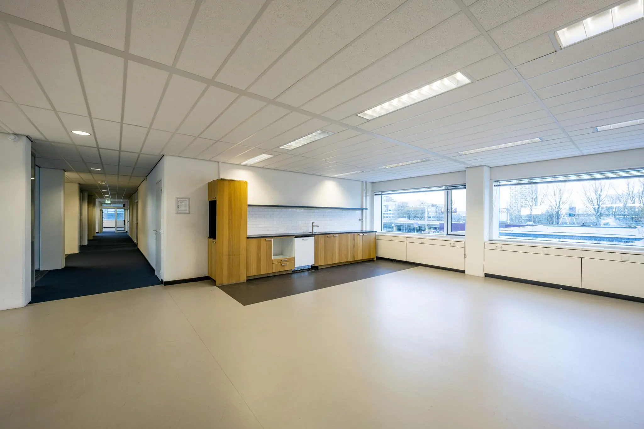 Lichte kantoorruimte aan de Spaklerweg met een kitchenette, grote ramen en uitzicht op een stedelijke omgeving.