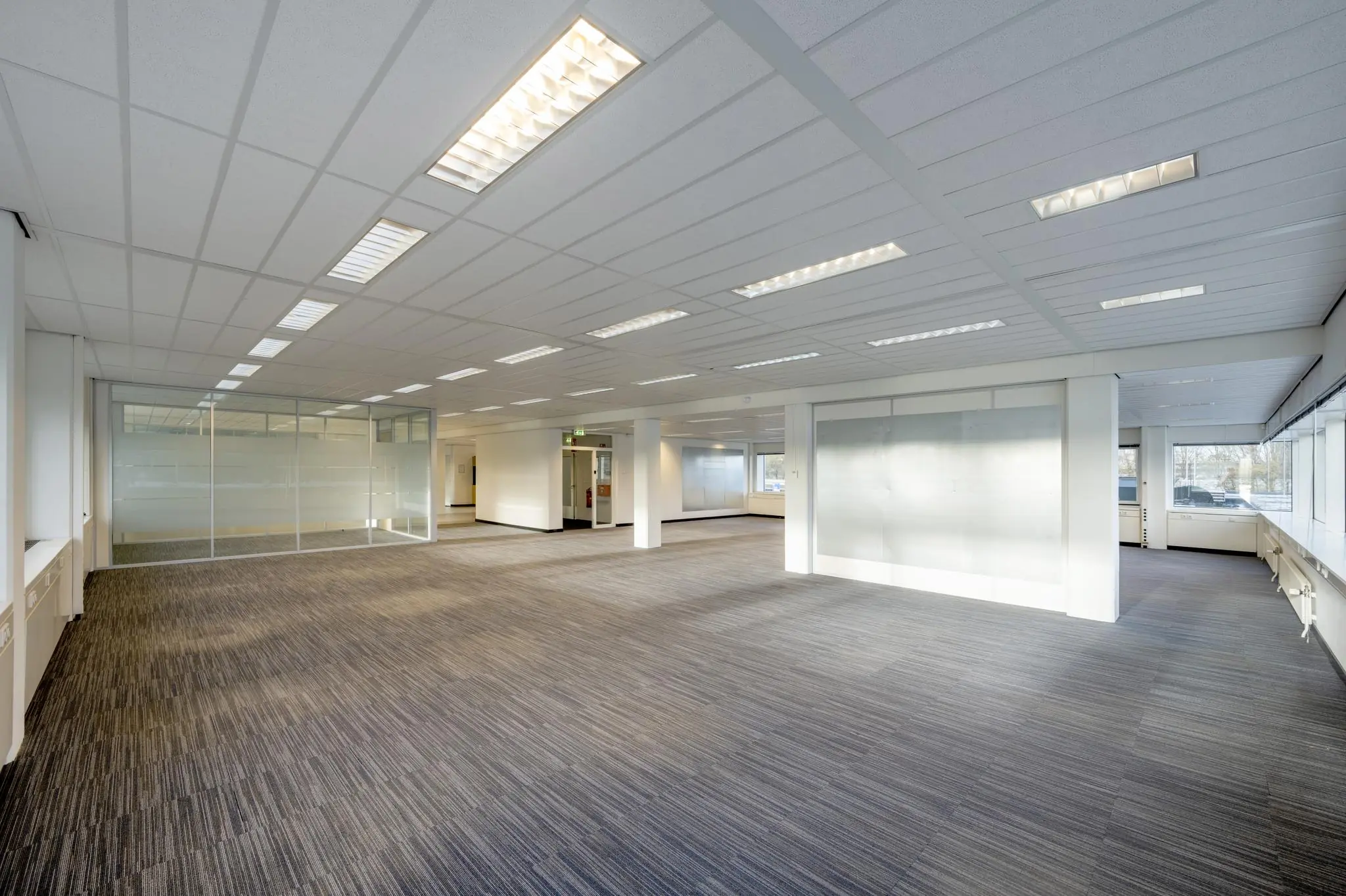 Ruime, lege kantoorruimte aan de Spaklerweg met tapijtvloer, systeemplafond en grote ramen.