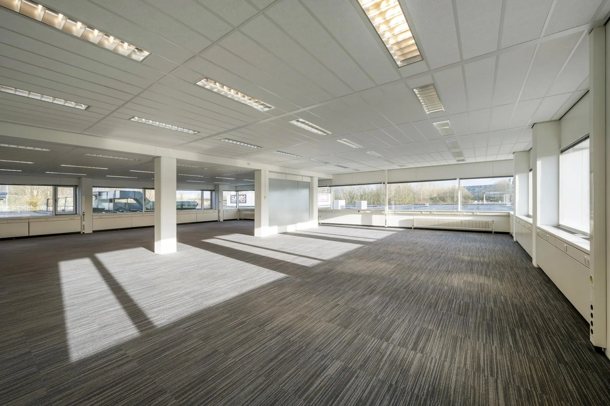 Lichte, lege kantoorruimte aan de Spaklerweg met grote ramen en grijze tapijtvloer.