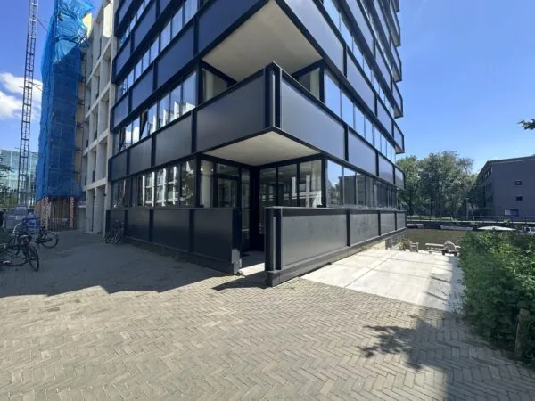 Zicht op de Willem Parelstraat met een modern zwart gebouw, een kanaal en een steiger op een zonnige dag.