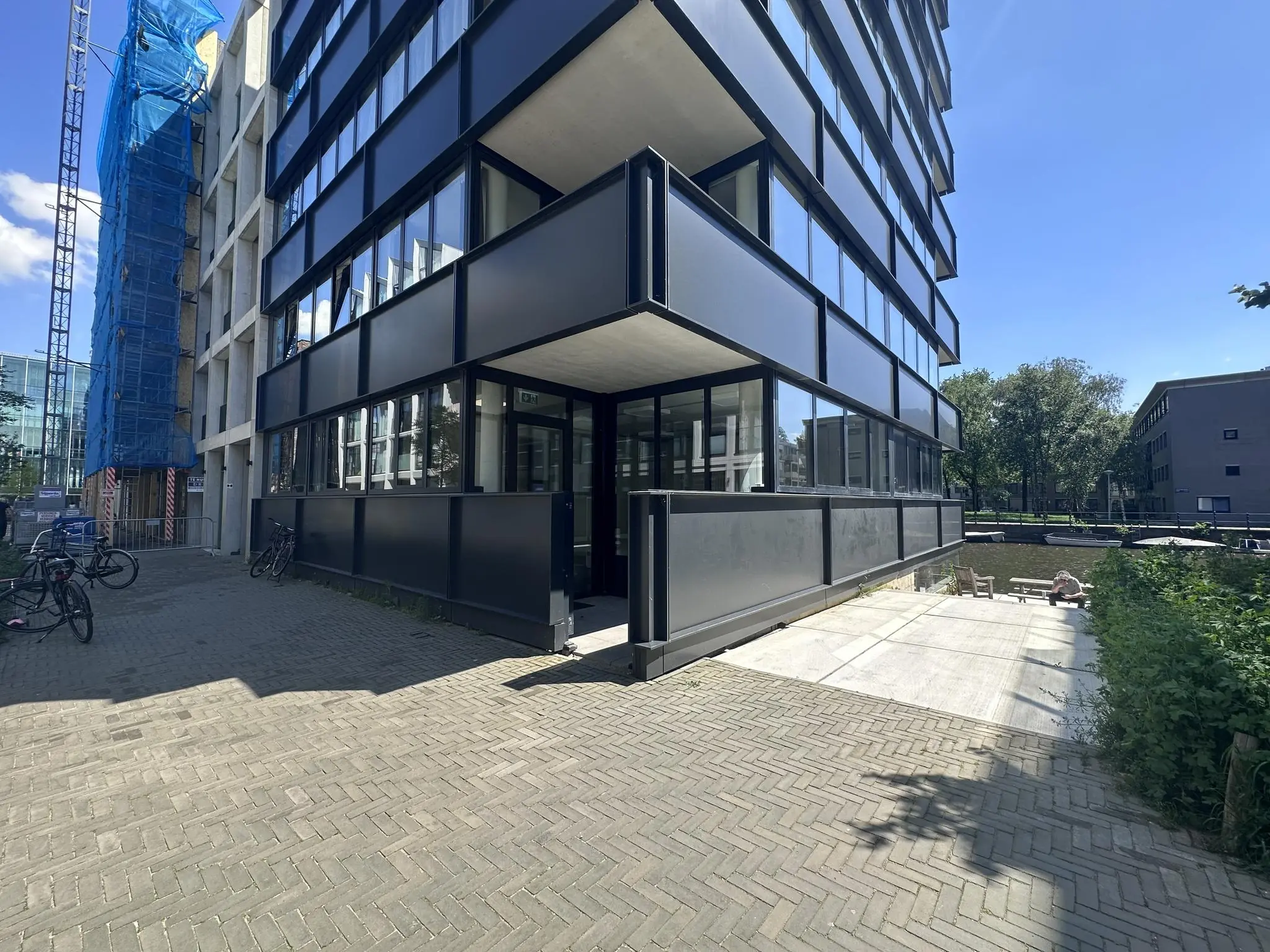 Zicht op de Willem Parelstraat met een modern zwart gebouw, een kanaal en een steiger op een zonnige dag.
