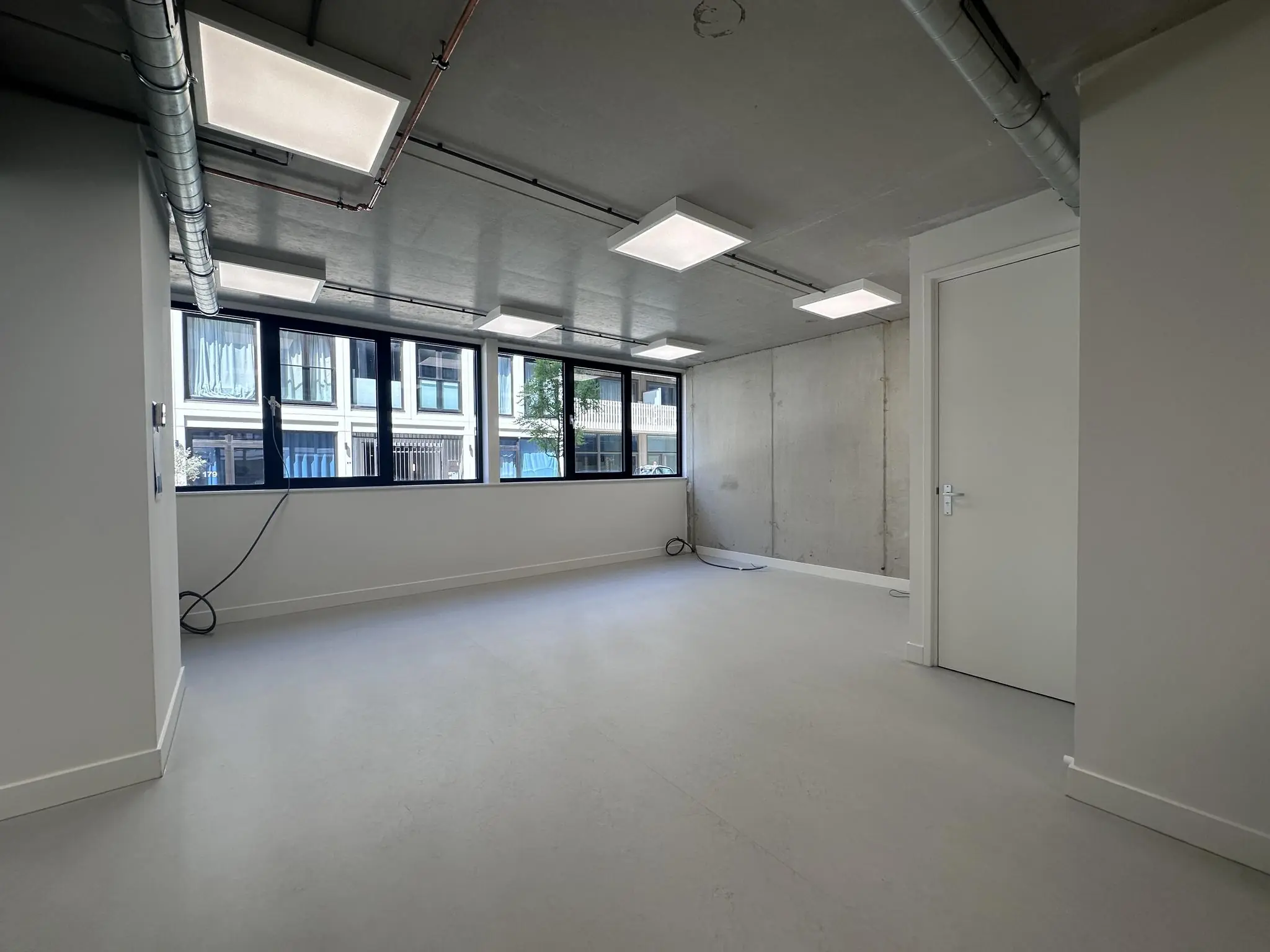 Leeg, modern kantoor- of bedrijfsruimte aan de Willem Parelstraat met betonnen muur, grote ramen en zicht op de straat.