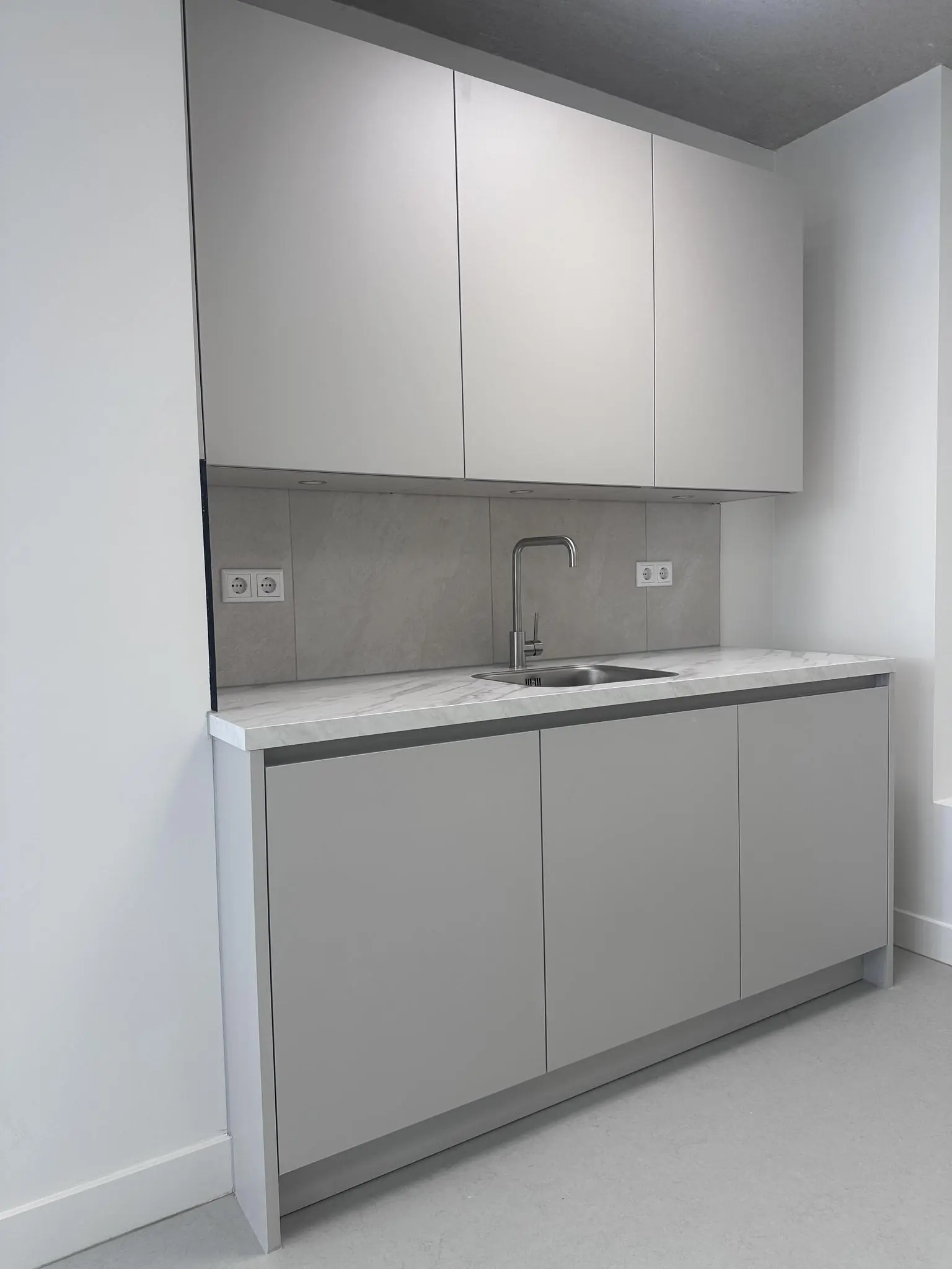 Moderne grijze kitchenette met boven- en onderkasten, een spoelbak en marmerlook aanrechtblad in de Willem Parelstraat.