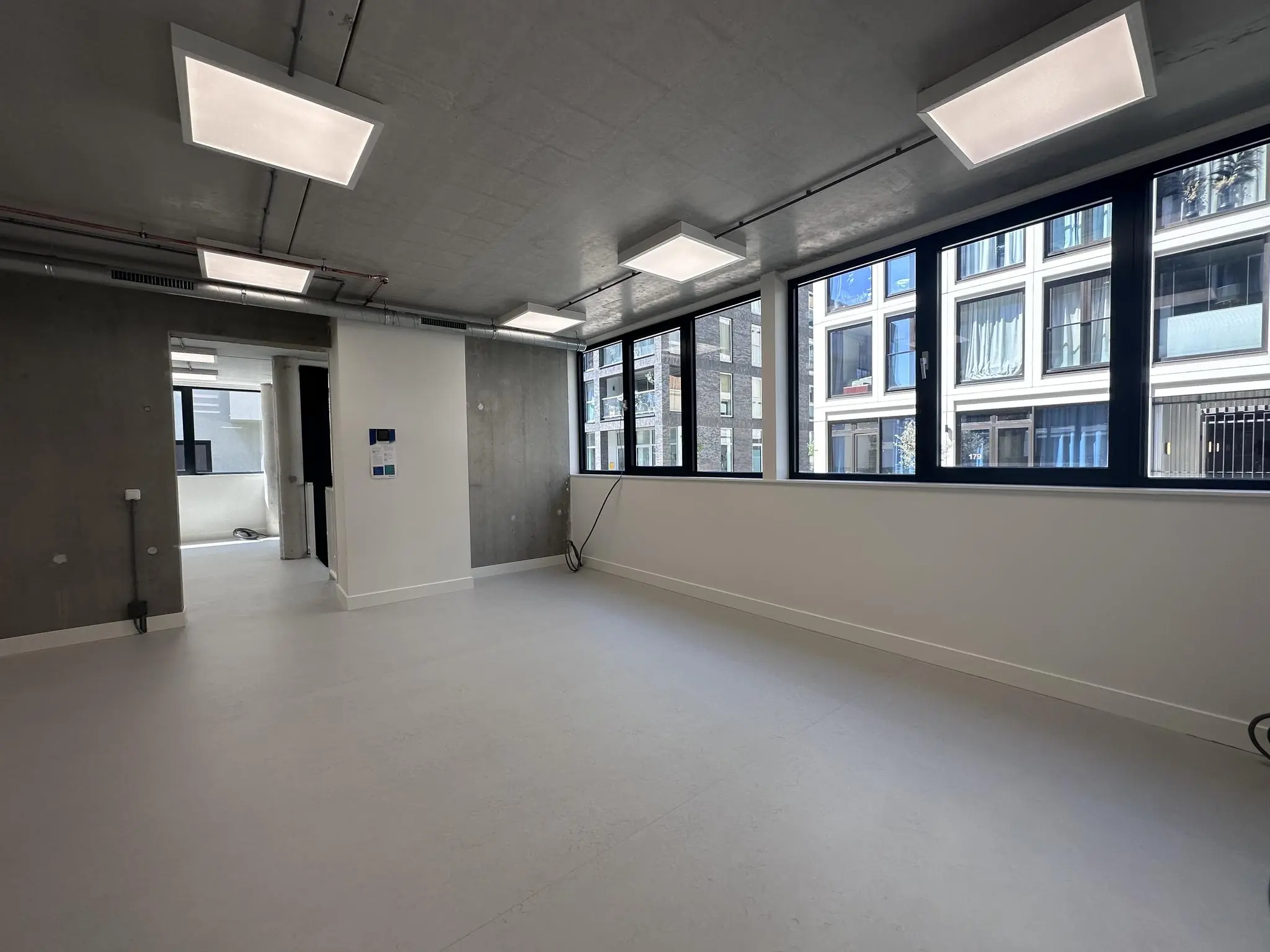 Lichte, lege kantoorruimte aan de Willem Parelstraat met grote ramen en zicht op tegenoverliggende gebouwen.