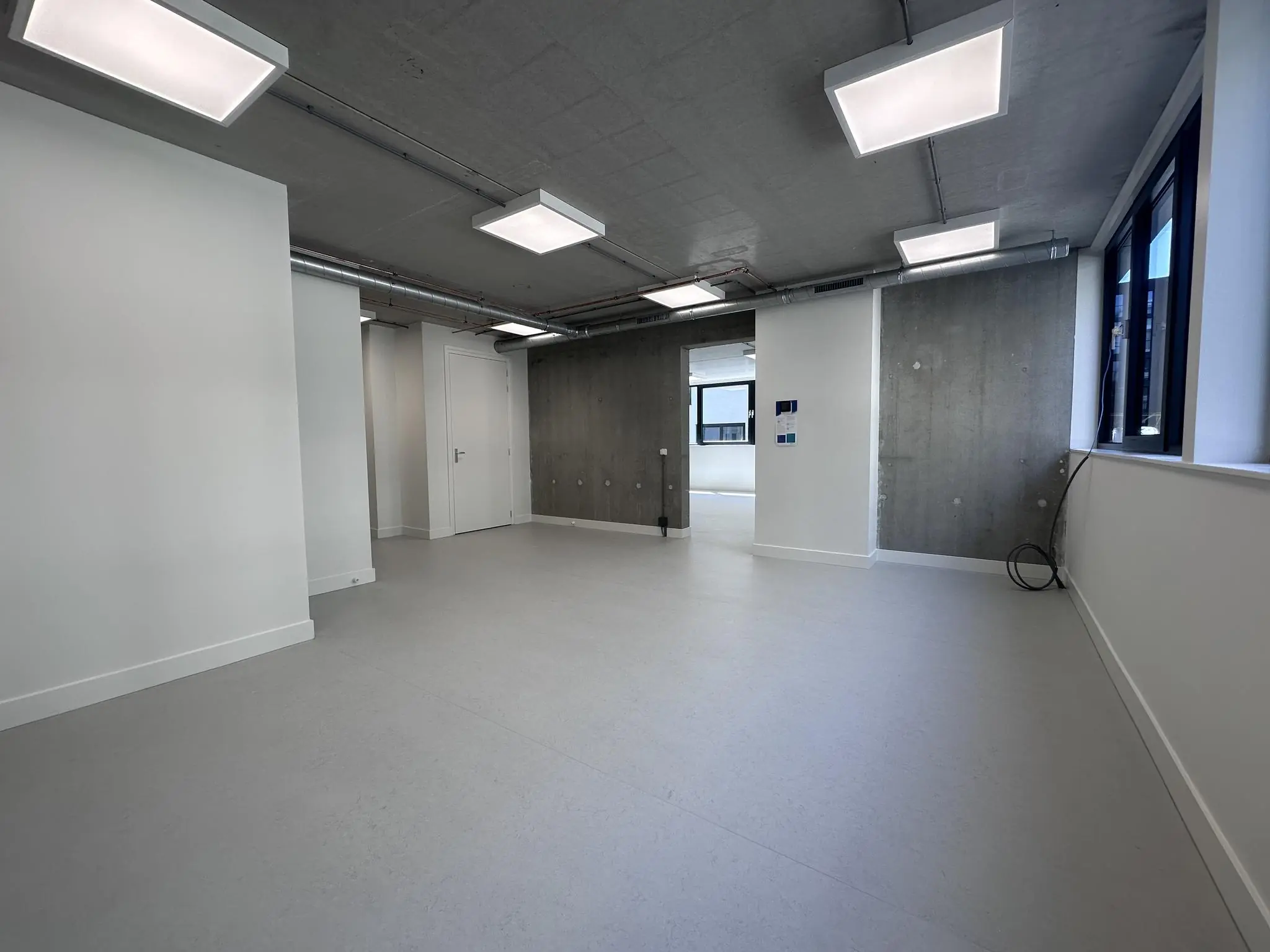 Lege, moderne kantoorruimte aan de Willem Parelstraat met betonnen muren en plafond, grote ramen en ingebouwde verlichting.