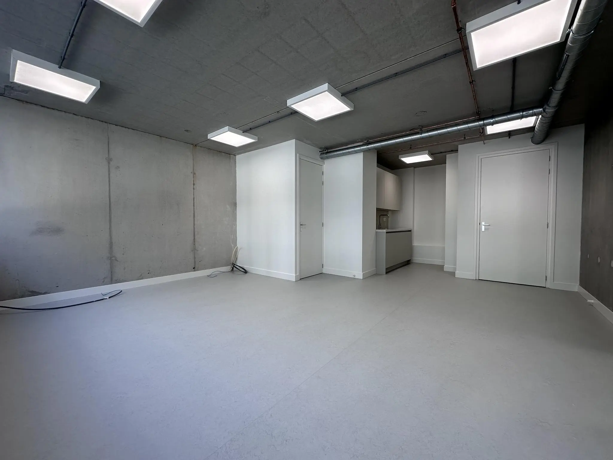 Leeg, modern afgewerkt appartement aan de Willem Parelstraat met betonnen muur, witte deuren en ingebouwde keukenhoek.