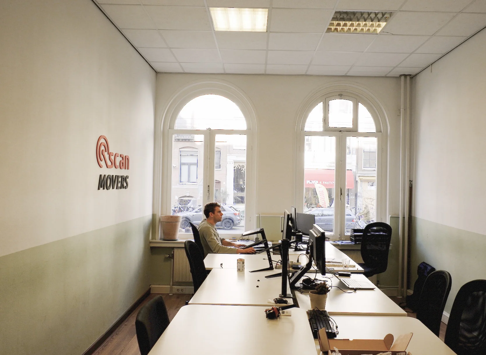 Kantoorruimte van Scan Movers aan de Raadhuisstraat met een werkende man achter meerdere computerschermen.